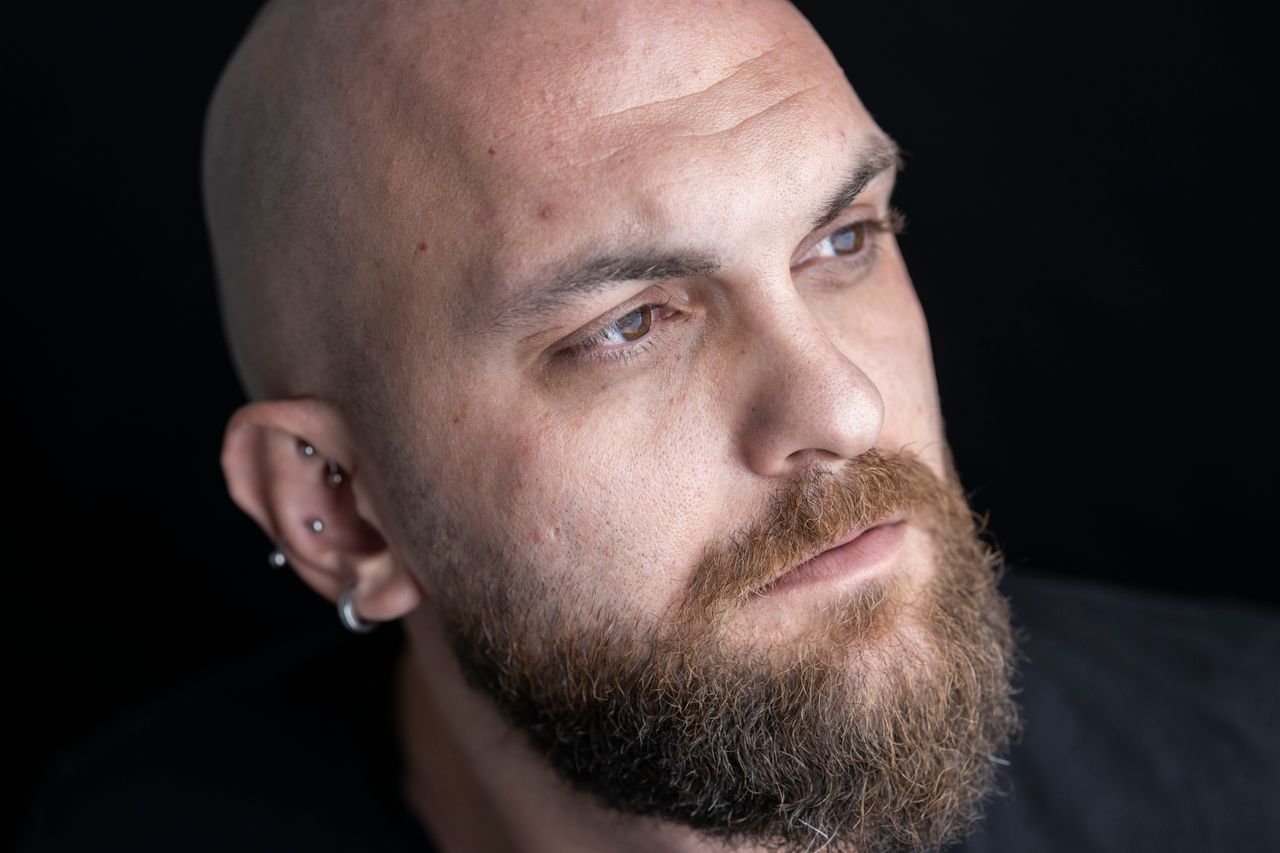 A detailed close-up portrait of a bald man with a beard and piercing, showcasing emotion and introspection.